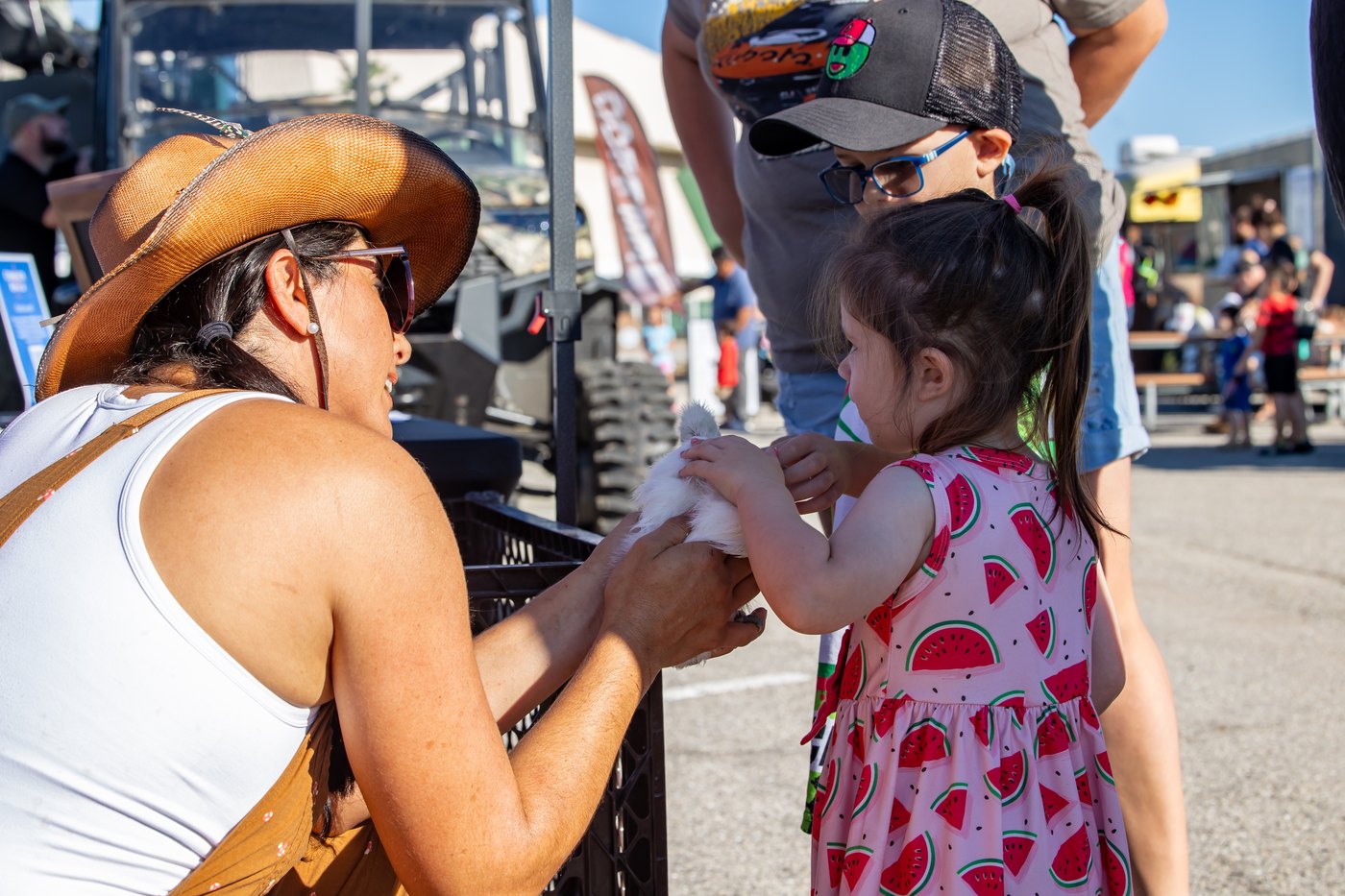 A child in a patterned dress gently touches a fluffy chicken with guidance from a Conquer Ranch handler.