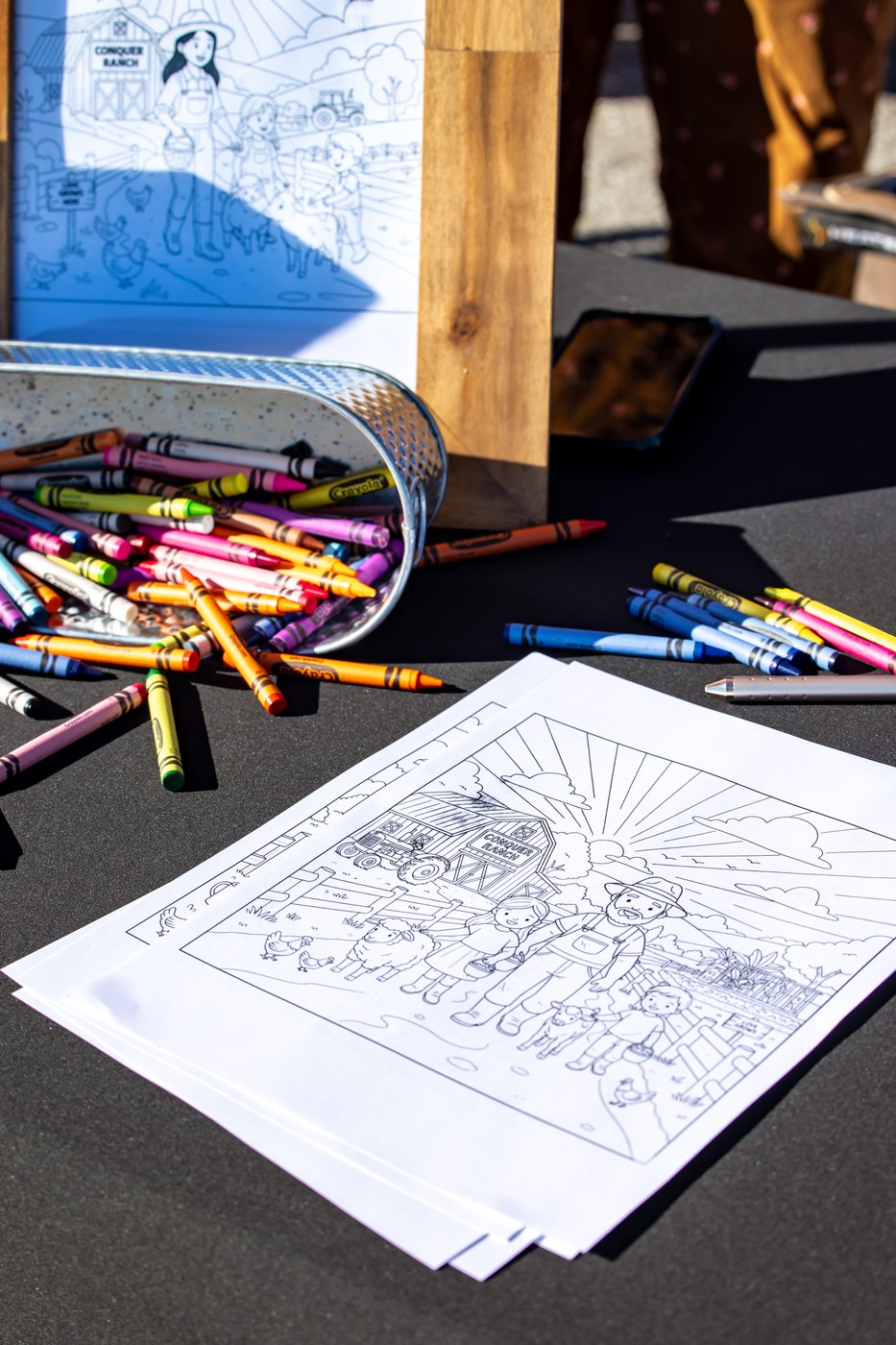 Coloring pages, crayons, and a framed ranch illustration are arranged on the Conquer Ranch activity table.