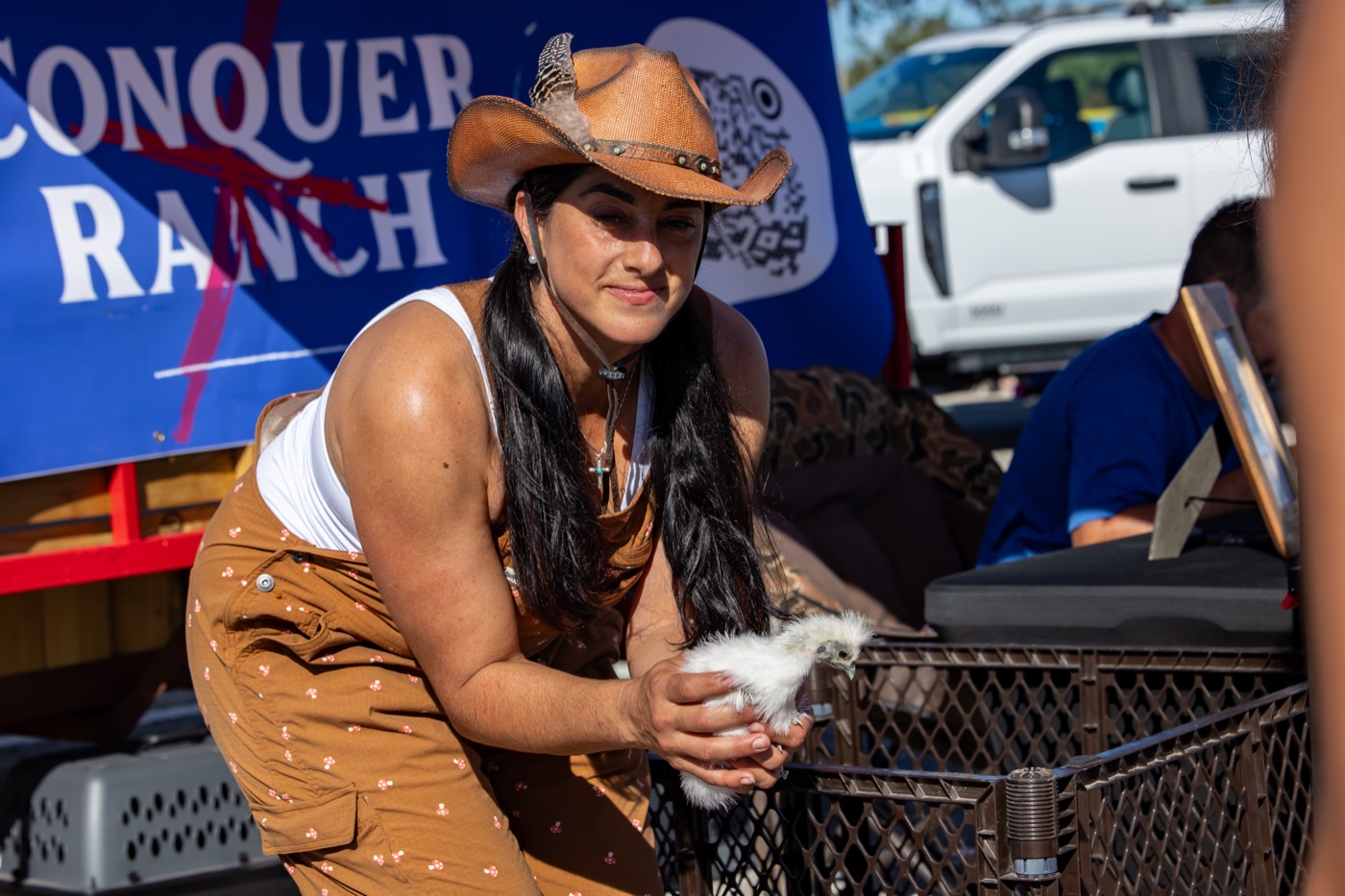 A handler holding a chicken in front of the Conquer Ranch banner