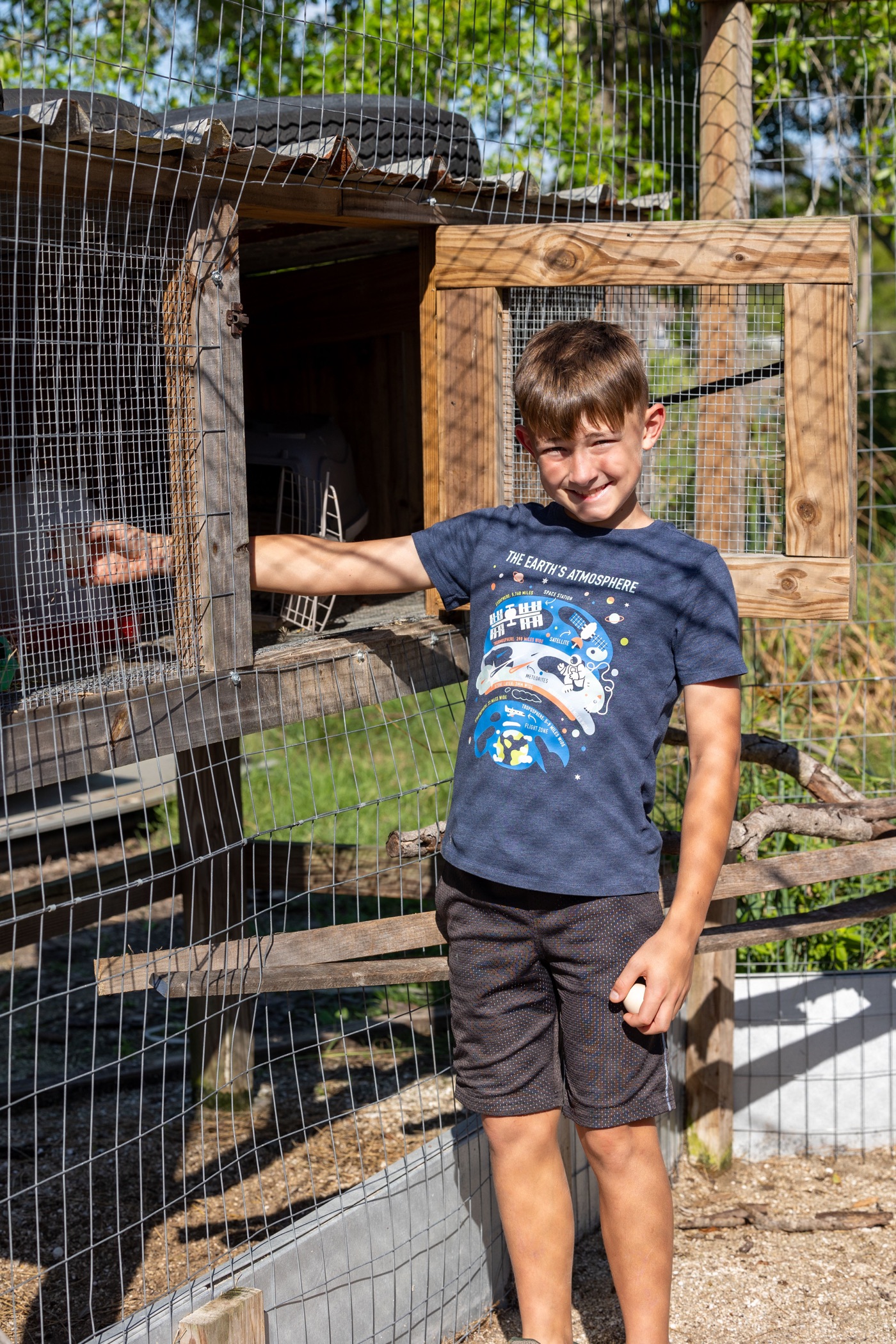 A child standing beside an animal enclosure at Conquer Ranch