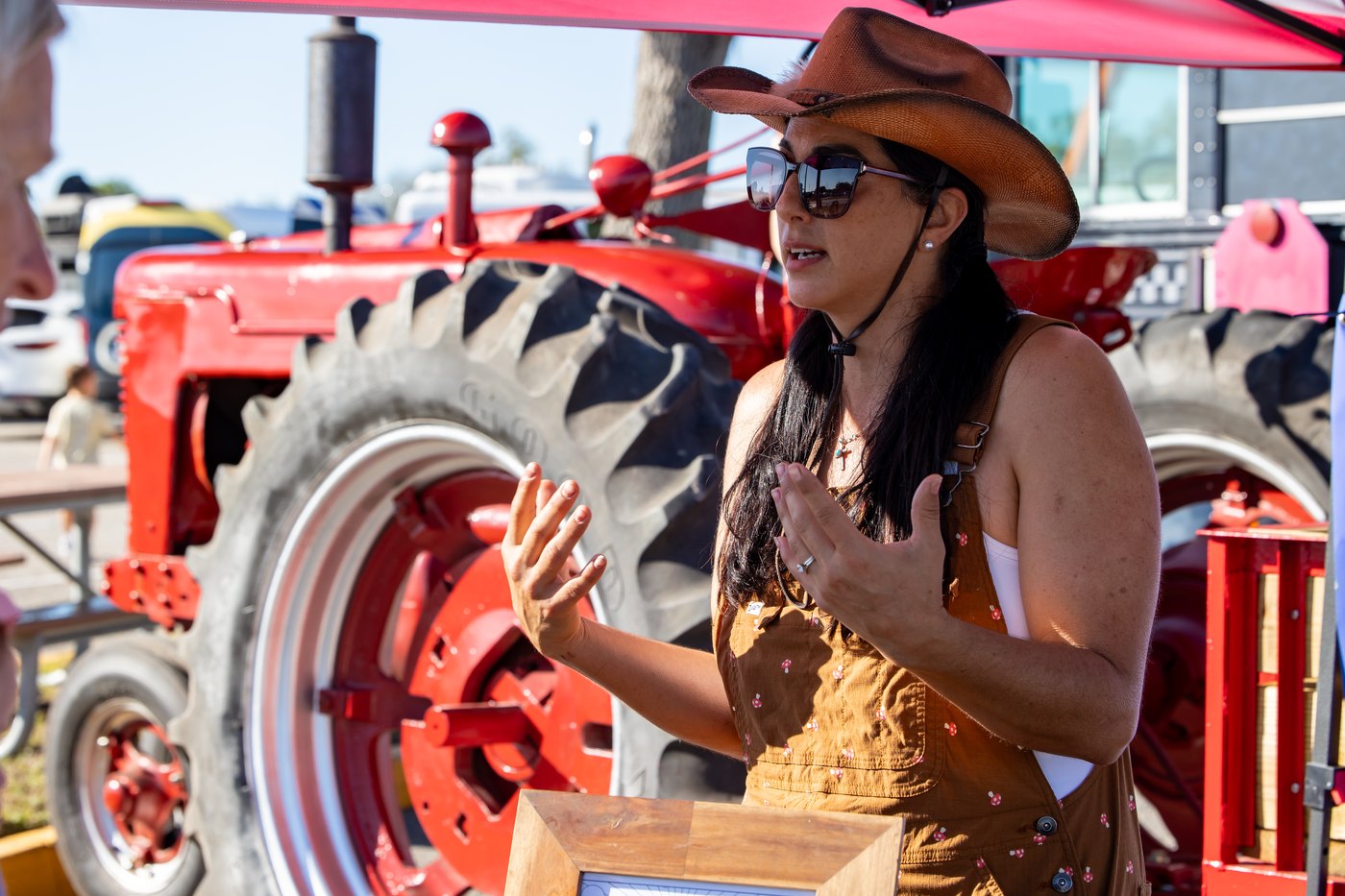 A Conquer Ranch handler in a cowboy hat talks with visitors beside the red tractor.
