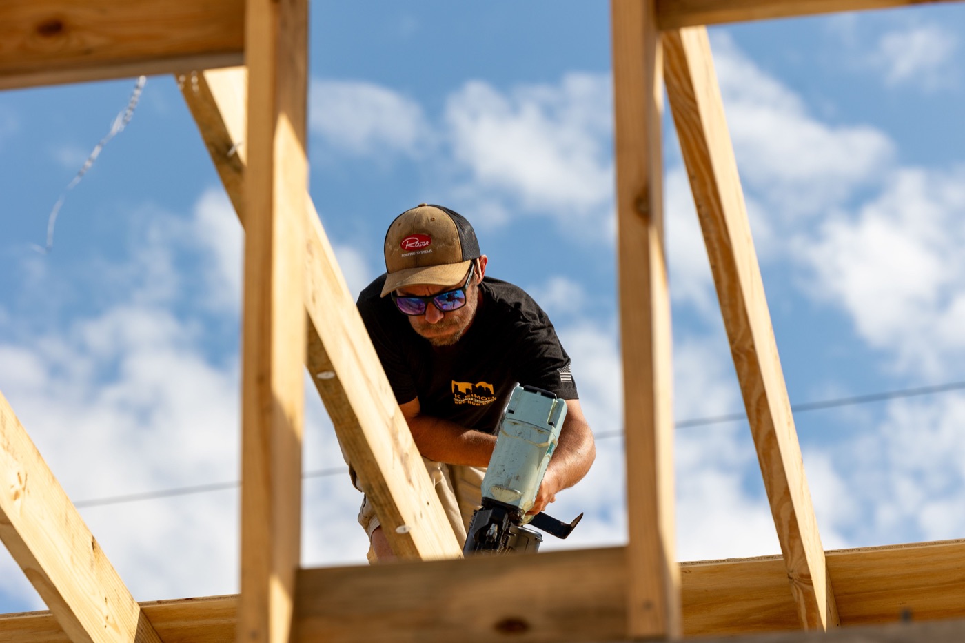 A person fastening timber roof framing beneath the blue sky